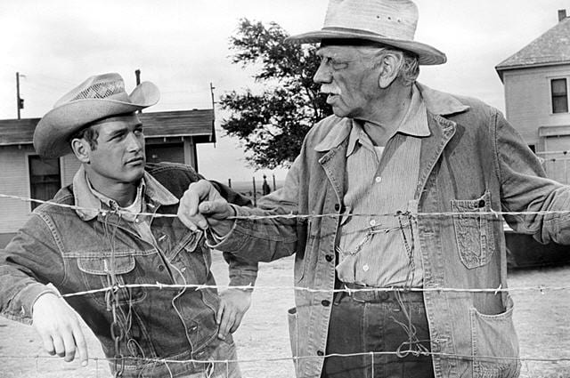 Paul Newman and Melvyn Douglas rest against a barbed wire fence