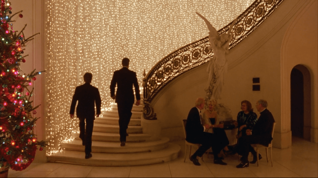 Two men walk up an ornate staircase decorated with a curtain of Christmas lights