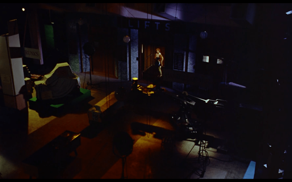 A woman walks into an empty movie set that is illuminated by pools of colored lighting