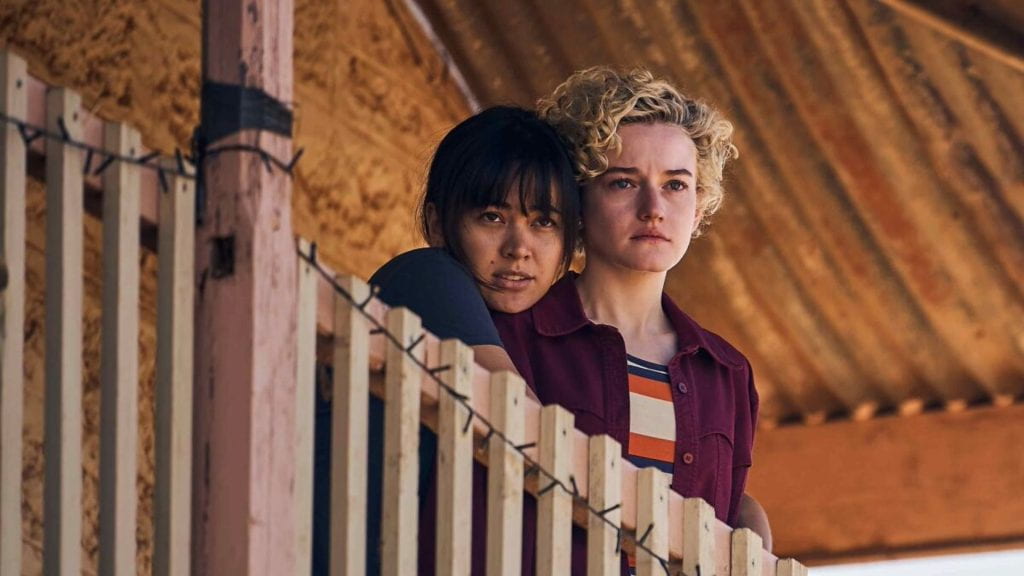 Jessica Henwick hugs Julia Garner from behind as they look over a deck railing