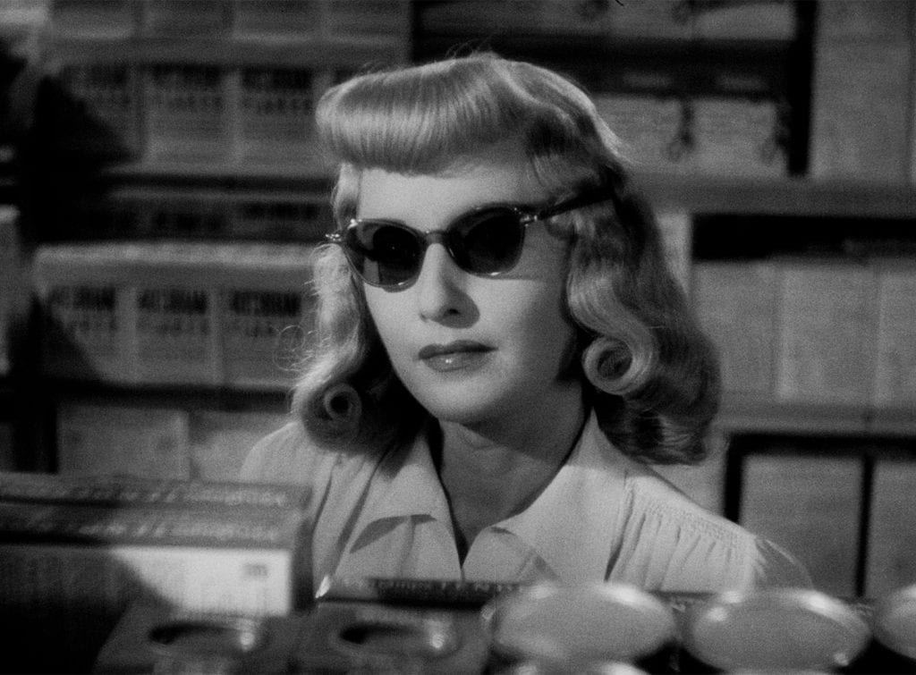 Barbara Stanwyck wears sunglasses and stares down Fred MacMurray in a supermarket