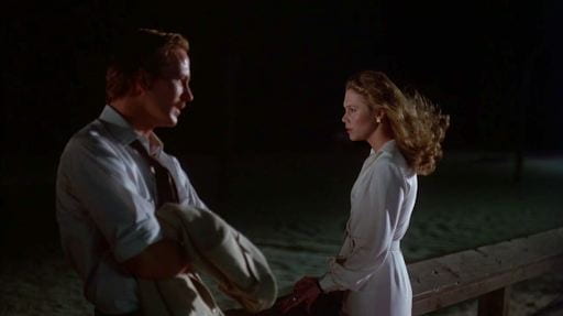 William Hurt and Kathleen Turner stand on a deck overlooking the ocean at night