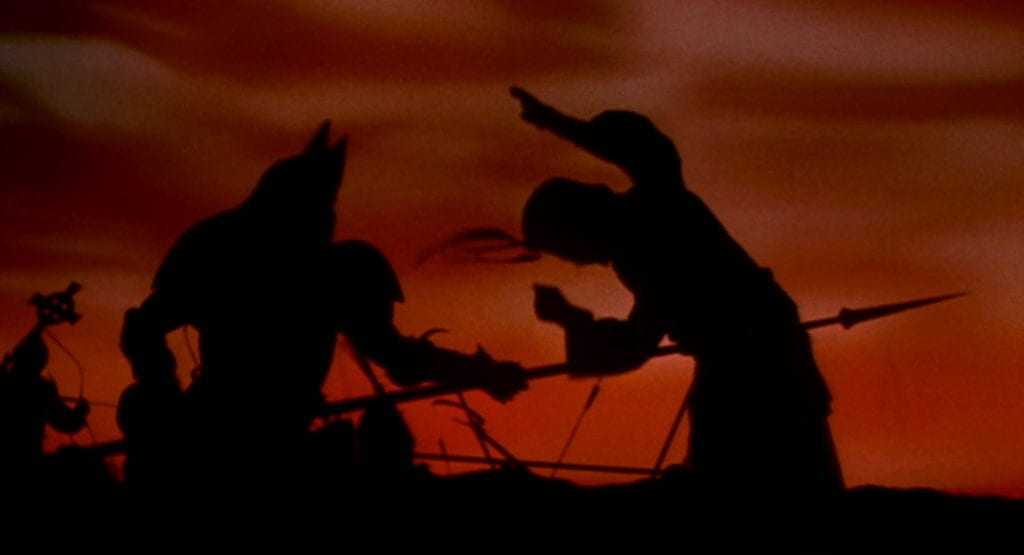 A silhouetted Dracula drives a spear into a soldier with an orange sky in the background