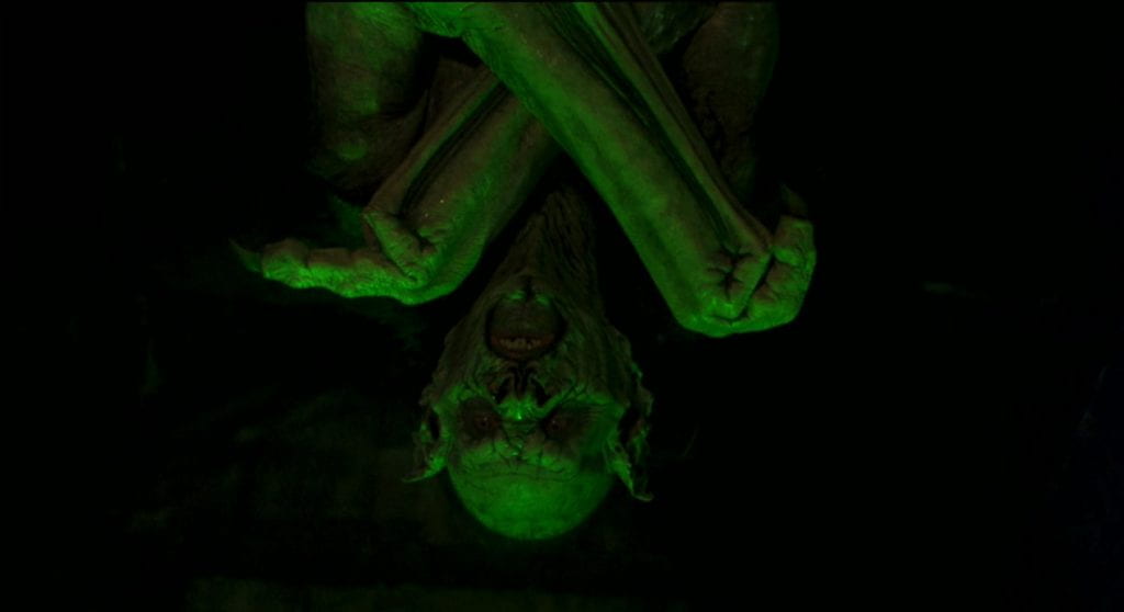 Dracula hangs upside down in his grotesque form, bathed in green light