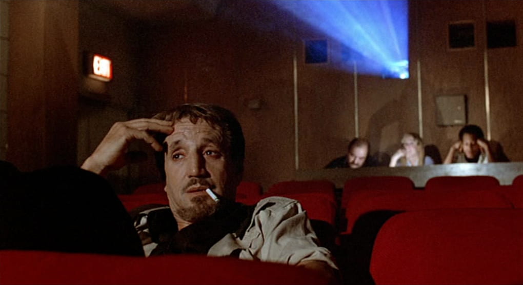 Joe sits in a screening room, watching a film while smoking