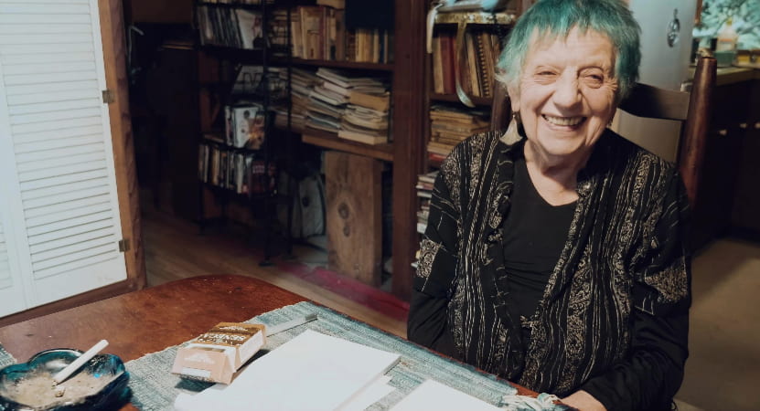 ruth weiss smiles at a table covered in papers