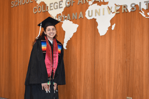 Sofia in graduation regalia next to wall in HLS with world map