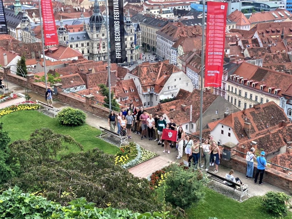 An aerial view of students holding an IU flag on a terrace overlooking an Austrian city