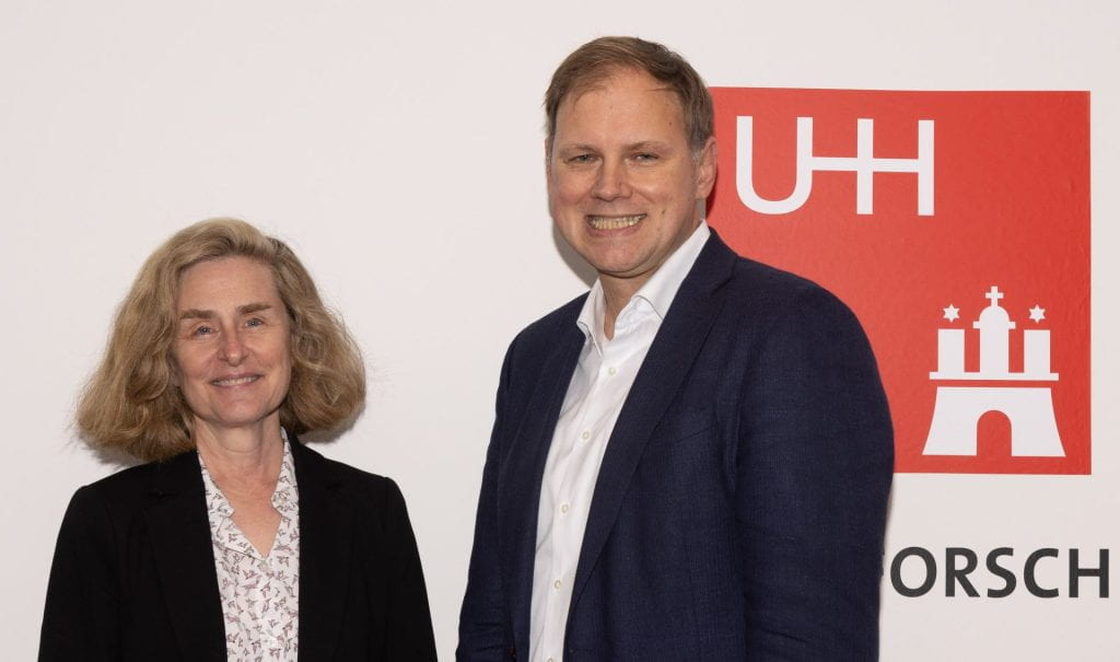 President Whitten and Heekeren smile at the camera in front of a white backdrop with the UHH logo in the background.