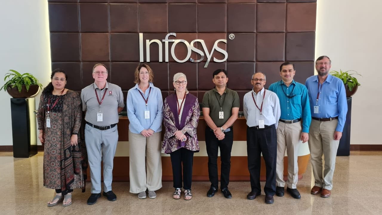 A group of people wearing lanyards stand in front of an Infosys logo