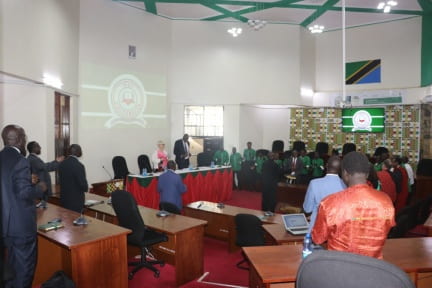 A large room decorated with Moi University logos, filled with people in formal dress.