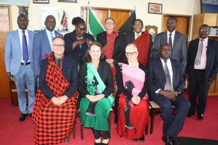 11 people stand and sit in two rows wearing suits and traditional Kenyan wraps.
