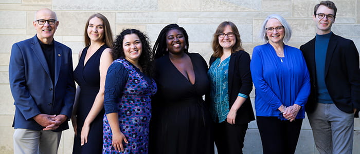 OECD Team members standing in front of a stone background dress in shades of blue. From left to right, Alain Barker, Faith Kopecky, Ella Torres, Maisah Outlaw, Jamey Guzman, Joanie Spain, and Kearsen Erwin.