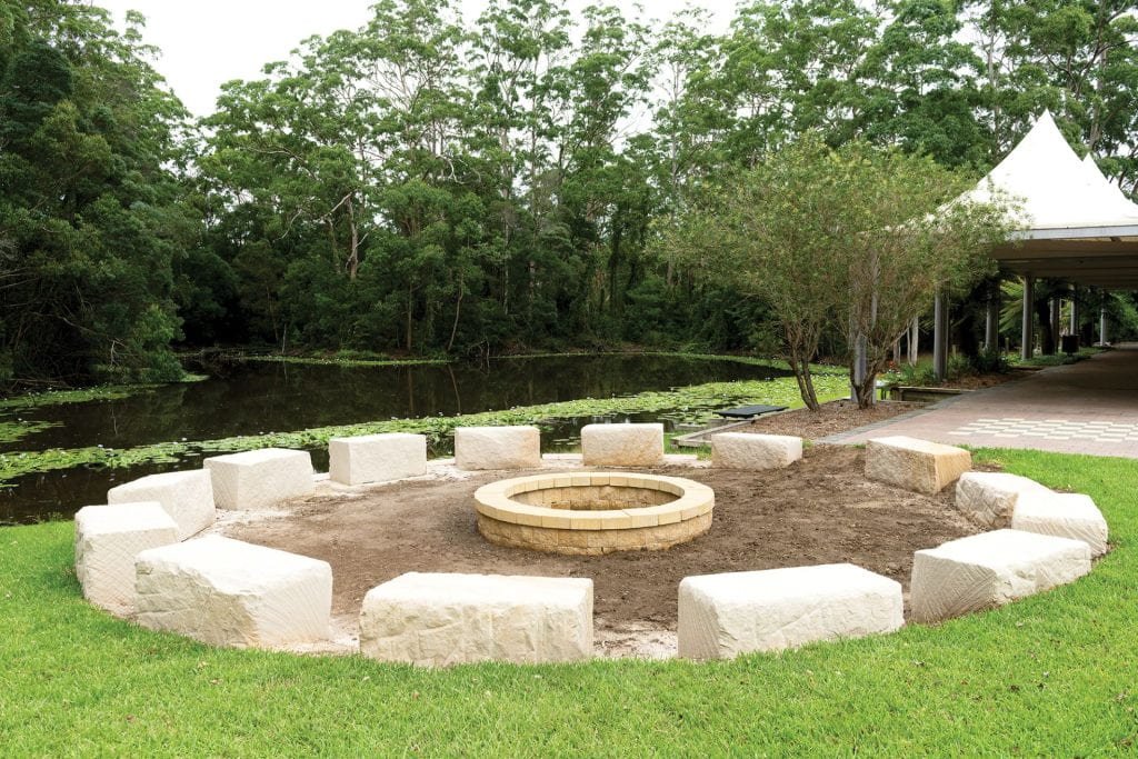 Image is of large stones for seating arranged in a circle around a stone fire pit.