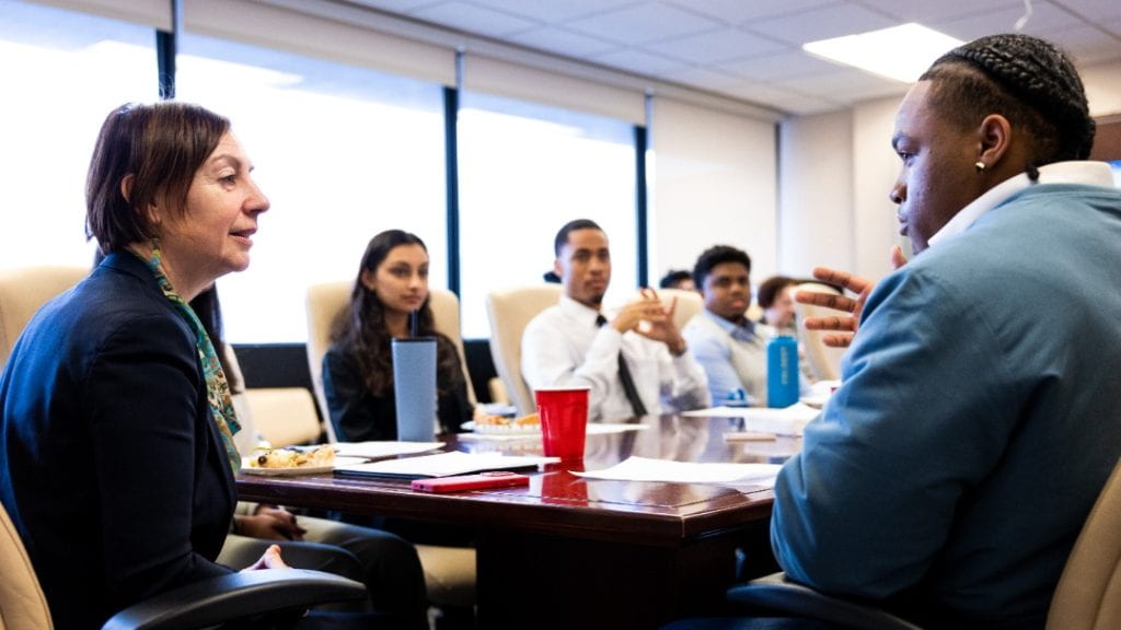 Female dean in professional dress speaks with multiple students around a conference table