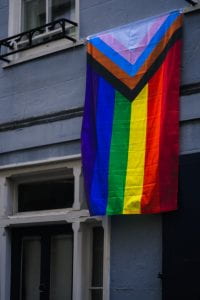 Inclusive Pride Flag hanging on a building. Photo by Just Jack on Unsplash.