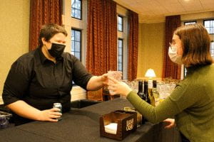 Bartender serving a drink to a woman, both masked