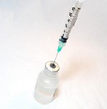 A syringe is inserted into a vial of vaccine.