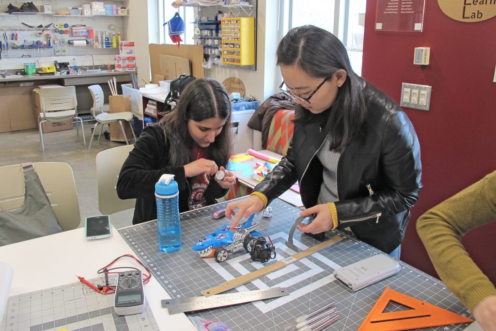 Two graduate students are at a table in the MILL working on building a small robot