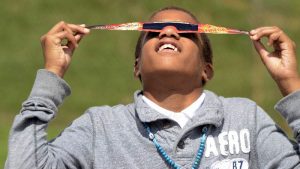 A boy looking up at the Sun through solar eclipse glasses.