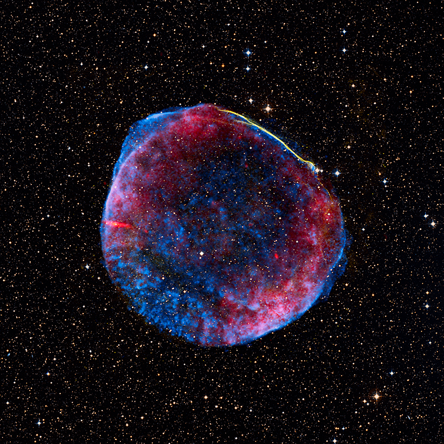 Against a backdrop of stars, a semi-transparent sphere of blue and red dust explodes outward from a central point. A thin line of yellow outlines a small section.