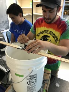 Two undergraduates are working on the device they created to measure the cardinal direction of flight of a moth. One undergrad is adjusting the moth attached to the device; the other undergraduate is checking the computer to make sure it is ready to record data