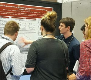 Richard Slivicki is surrounded by four on-lookers while he points at a graph on his poster at the Society for Neuroscience conference in 2016.