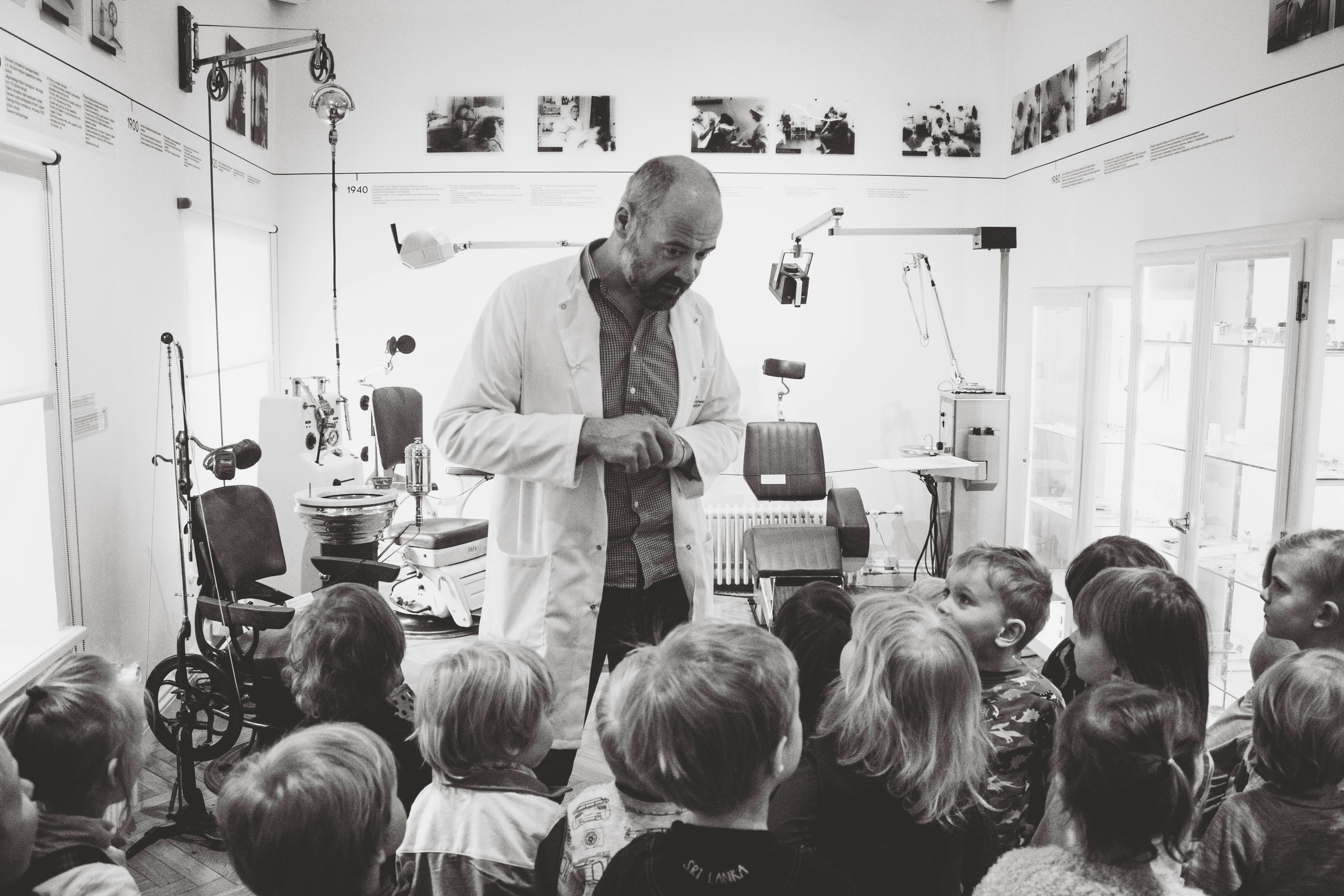 Man in lab coat lecturing to children in a medical setting.