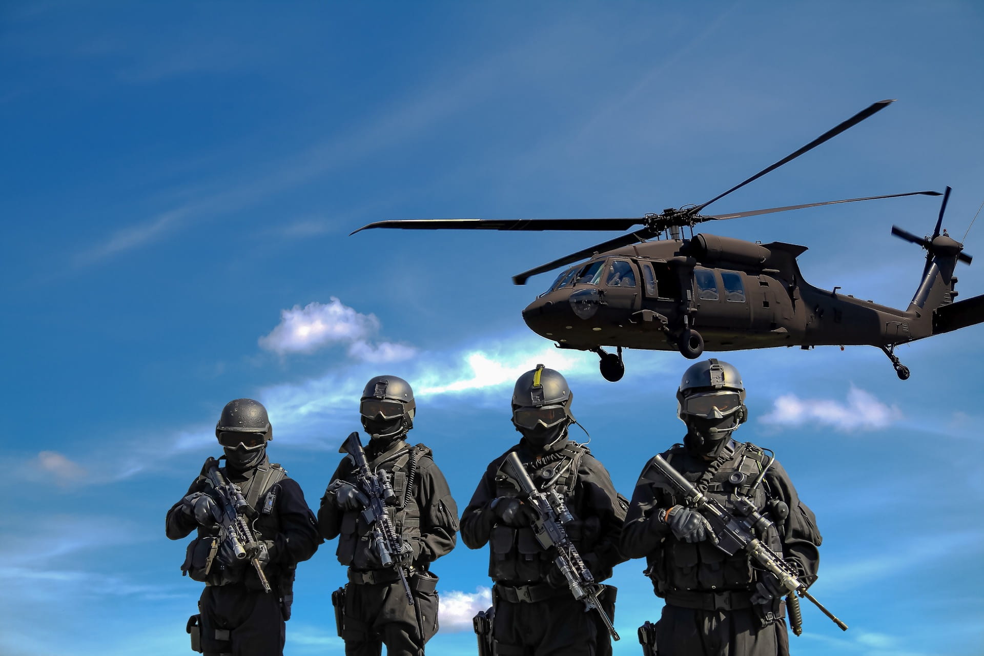  Four soldiers side by side in front of a low-flying helicopter.