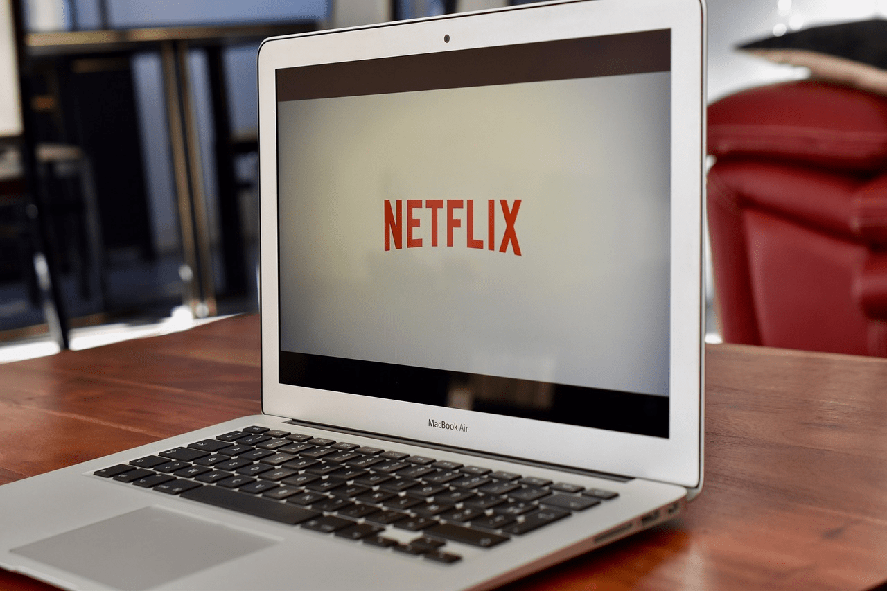 A laptop sits on a table, with its screen showing the Netflix logo.