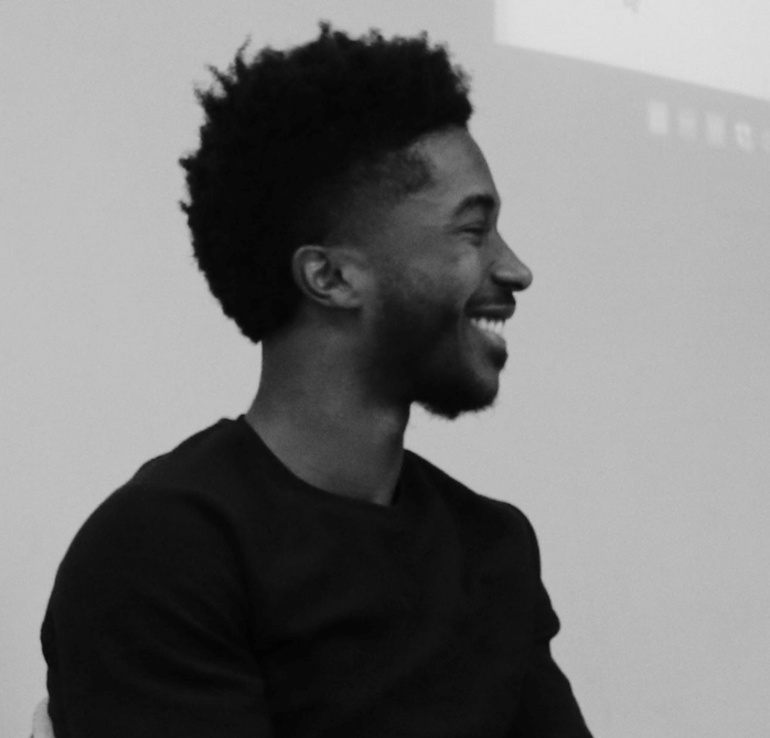 [DJ Purnell is captured from the side, smiling. He is sitting at a panel on advice for applying to graduate school]