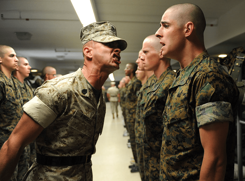 A U.S. Marine Corps drill sergeant yells at a lower-ranked Marine in front of others.