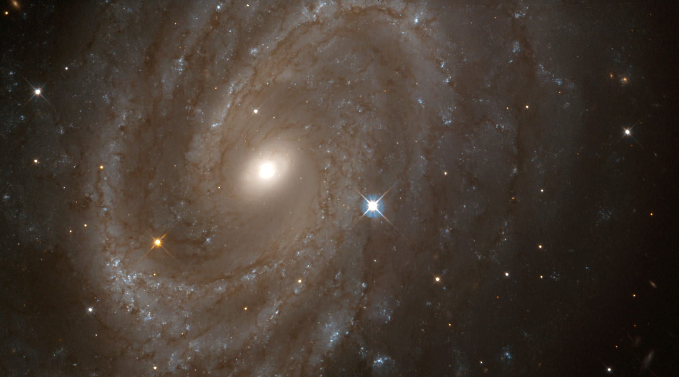 A spiral galaxy with multiple arms. Light blue arms against a black background with a bright white center. A bright, pale blue star to the right of the center is in stark contrast to the darker arms.