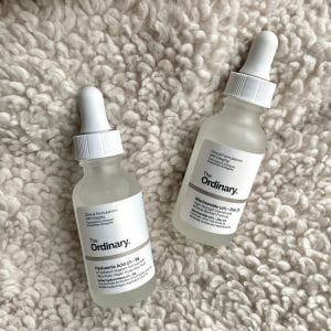 Pictured are two, small bottles with pipettes containing clear and viscous liquids. The bottle on the right contains hyaluronic acid and the bottle on the left contains niacinamide.