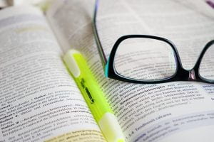 yellow highlighter set on an open textbook with black glasses on top of it