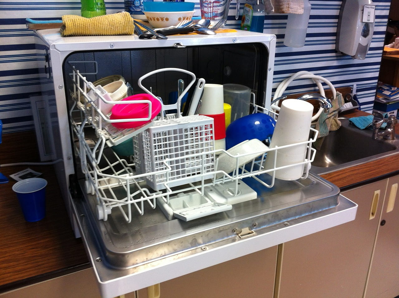A dishwasher sitting on a shelf that is open and showing itself as being full of dishes.