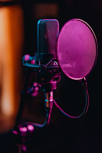 [Recording microphone with pop filter lit in soft purple light.]