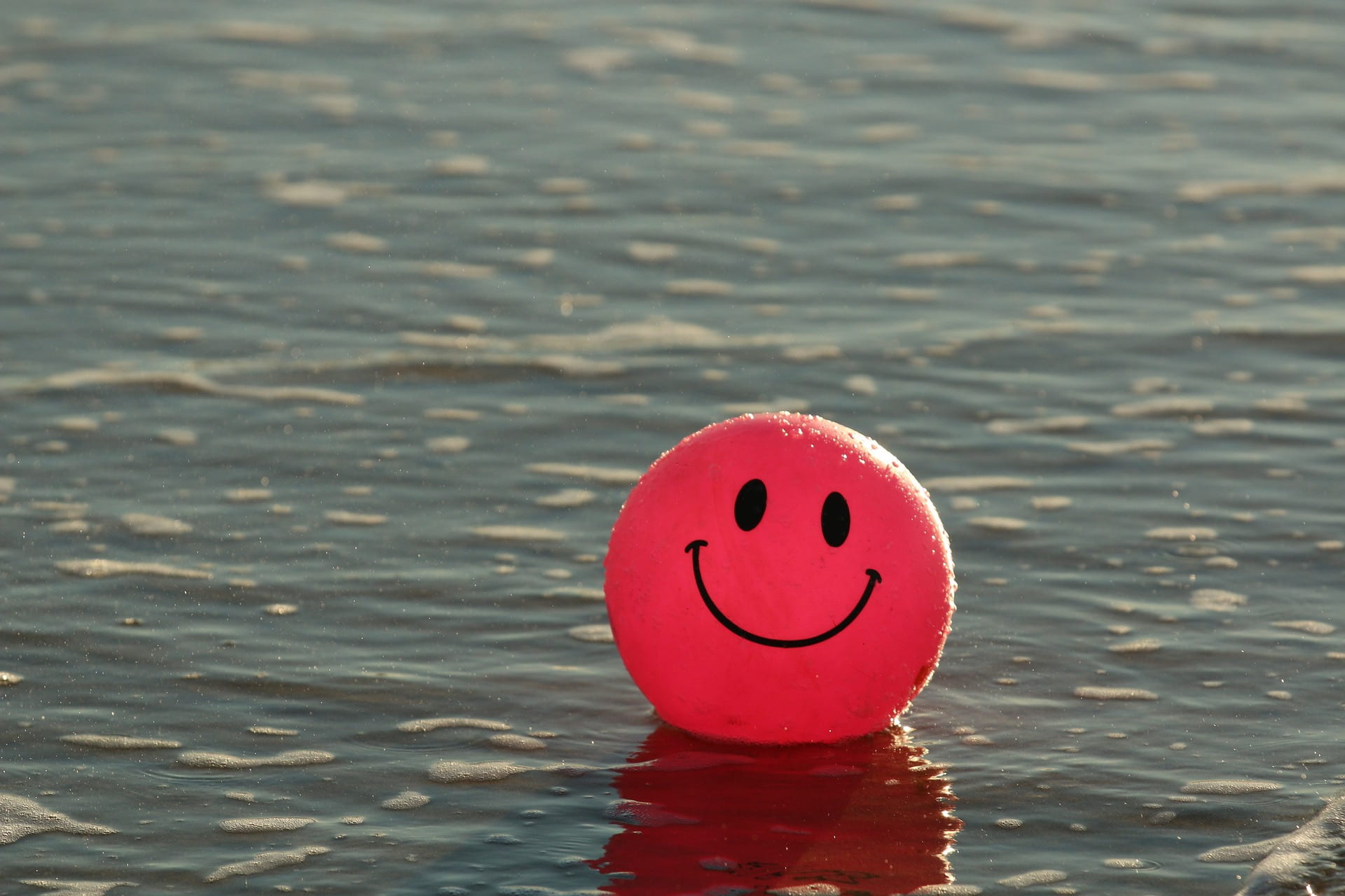  Image of a red ball with a smiley face on it, floating in water.
