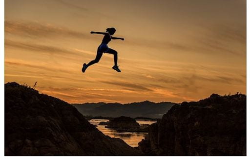 [Image of an individual jumping from one hillside to another during a sunset.]