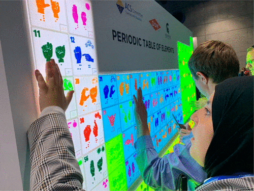 [Prof. Mona Minkara at the completed accessible, tactile 3D-printed Periodic Table in the exhibition hall at the National ACS meeting in San Diego, CA.]