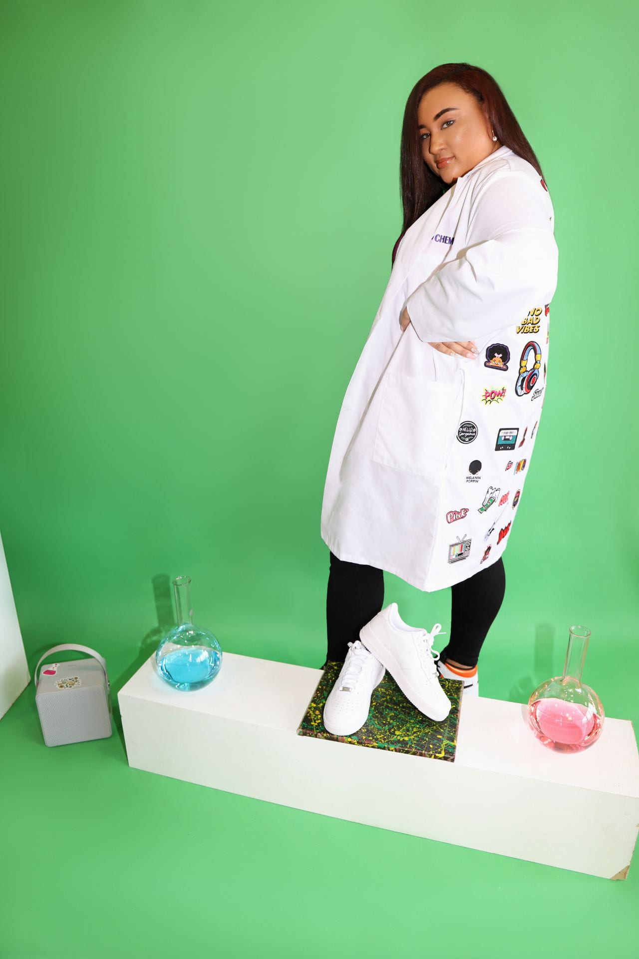 Picture of Jakyra Simpson wearing a lab coat, posing with sneakers and chemistry beakers. 