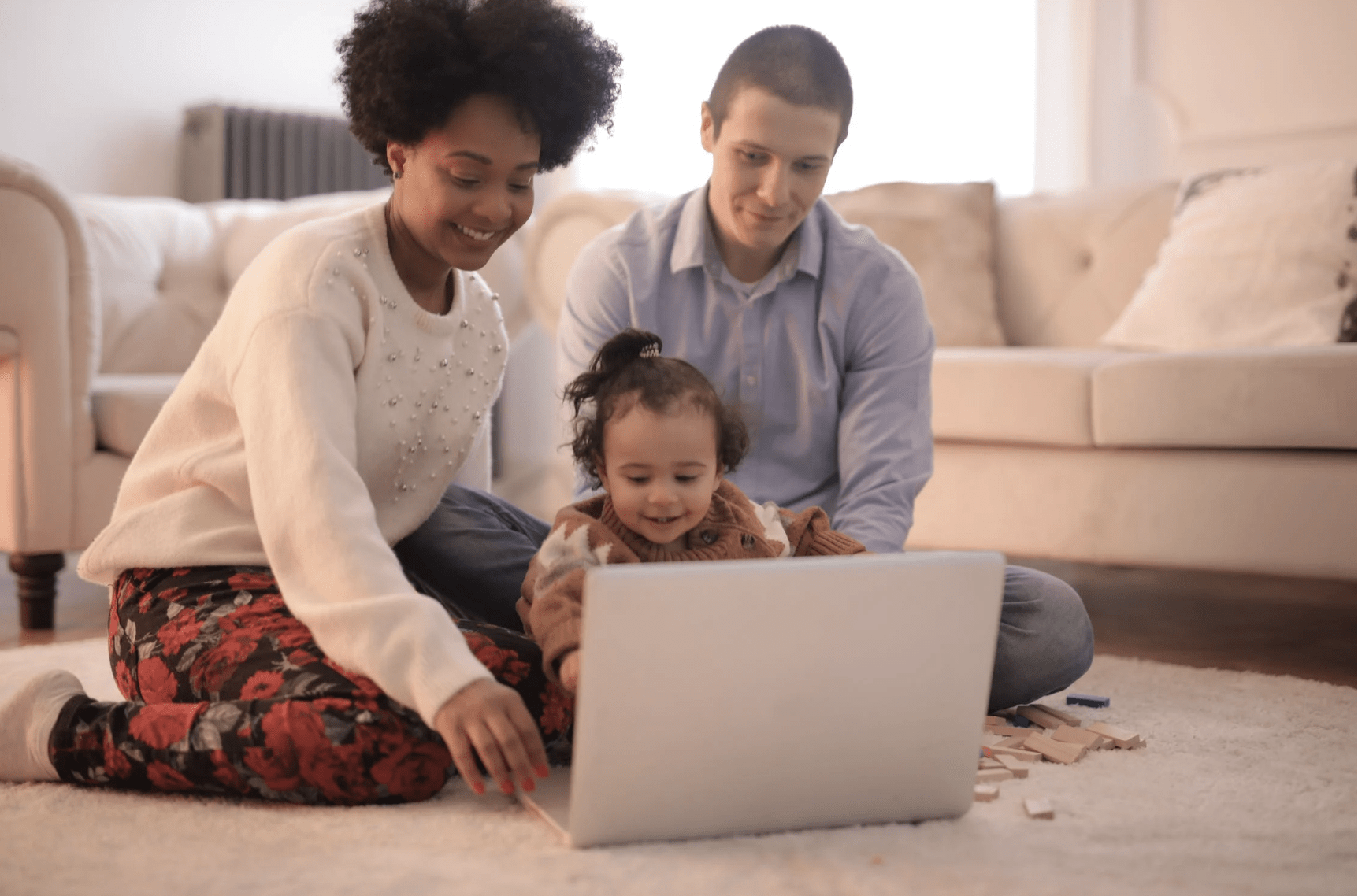 Parents and a young child joyfully playing together with a laptop and some building blocks.