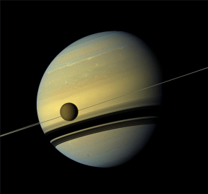 An image of Saturn with its moon, Titan. Saturn’s rings, below Titan, cast a shadow on the planet. 