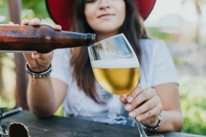 Photo shows a young woan pouring beer from a bottle to a glass.