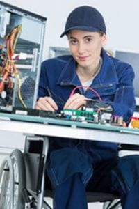 Young woman in a wheelchair sitting at a table and working on a circuit board.