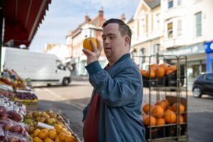 A man inspecting an orange at an outdoor fruit stand.